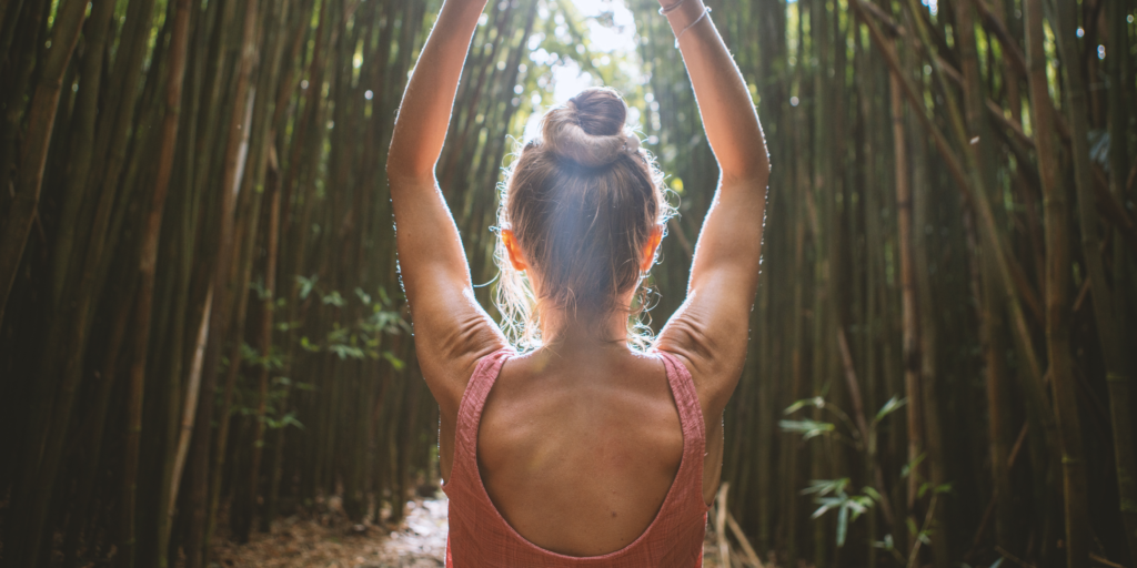 Girl in a bamboo forest wearing a yala bamboo top meditating with her arms up.