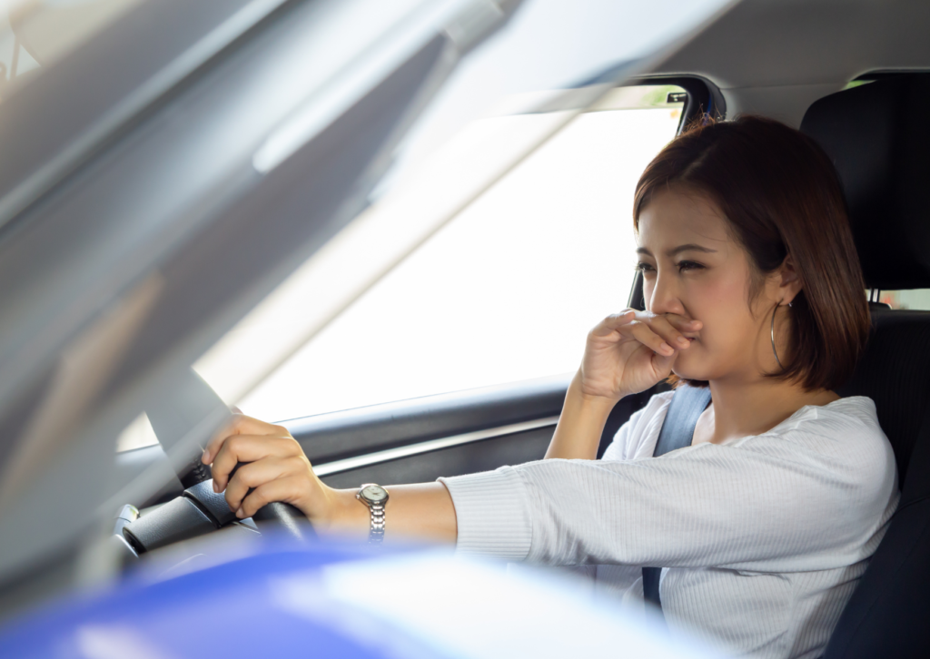 Woman in a car looking displeased with the air quality, considering the use of a non-toxic car air freshener.
